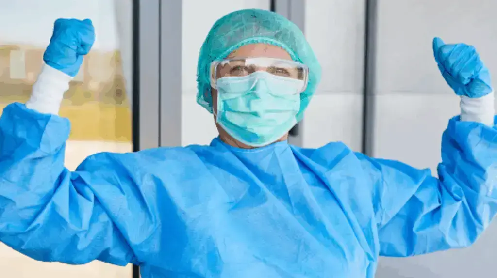 Nurse in protective gear raising arms in celebration.