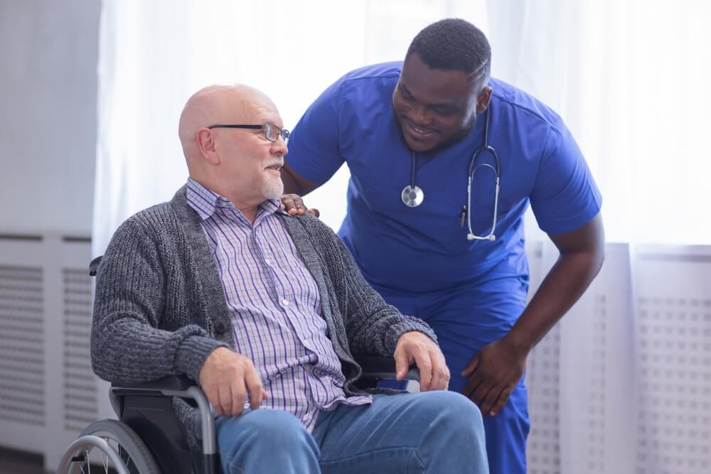 A male nurse leans down to talk to a male patient in a wheelchair