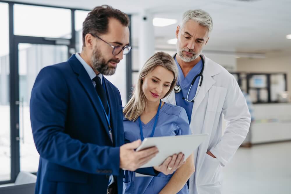 A man in a suit shows a tablet to two nurses