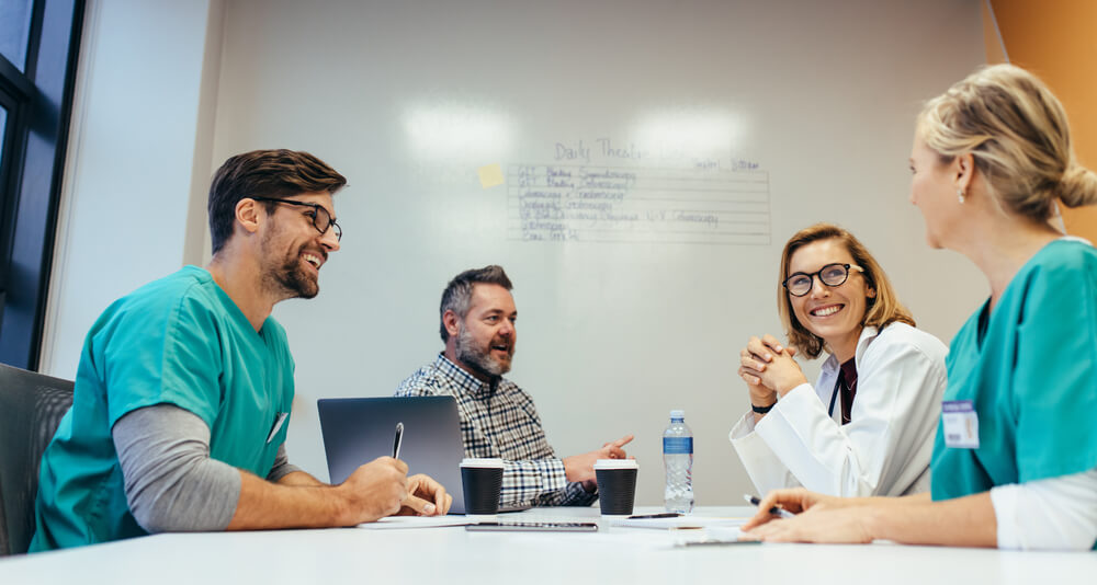 A group of doctors and nurses sit around a table, discussing and planning for the Magnet Recognition process.