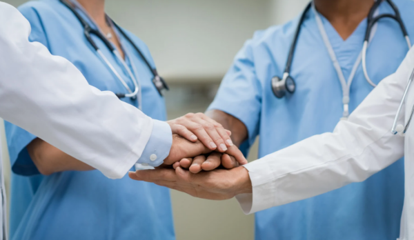 A diverse group of nurses and interprofessional clinicians gathered around a table in a unit setting, collaborating, reviewing data, or in a shared governance-style meeting. A diverse group of nurses and interprofessional clinicians gathered around a table in a unit setting, collaborating, reviewing data, or in a shared governance-style meeting.