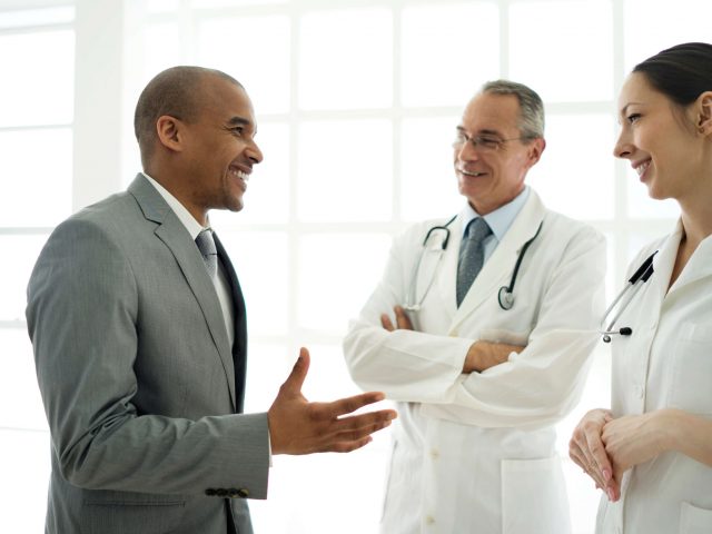 Male health care consulting partner chats with two doctors