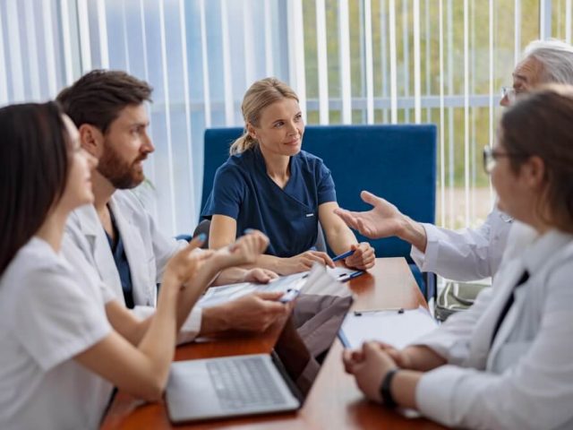 Team of doctors and nurses sit at a table with laptops in front of them