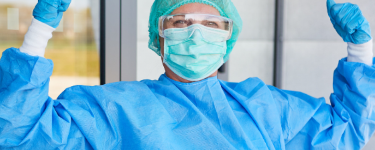 Nurse in protective gear raising arms in celebration.