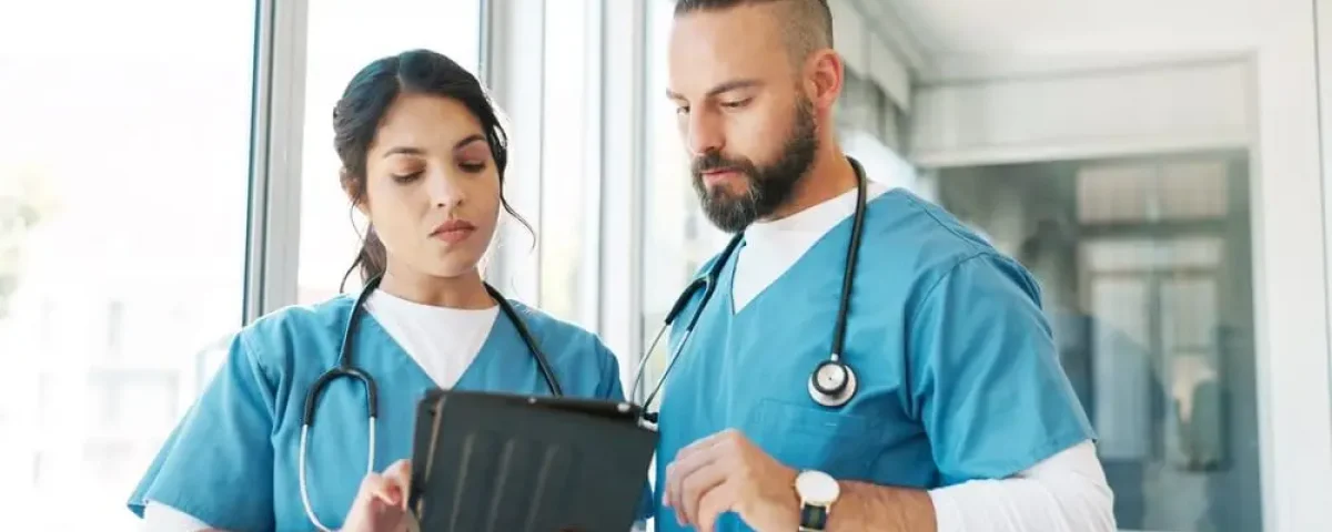 A male and female nurse in blue scrubs look at an iPad together